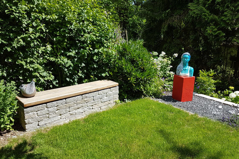 Gartenplanung mit Natursteinsitzmauer mit Holzauflage.