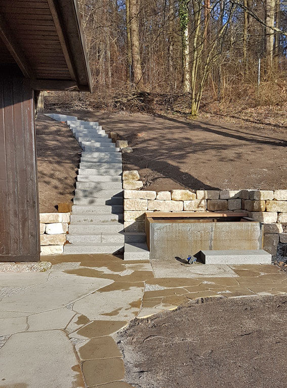 Gartengestaltung mit Natursteinmauer und modernem Wasserbecken aus Cortenstahl.